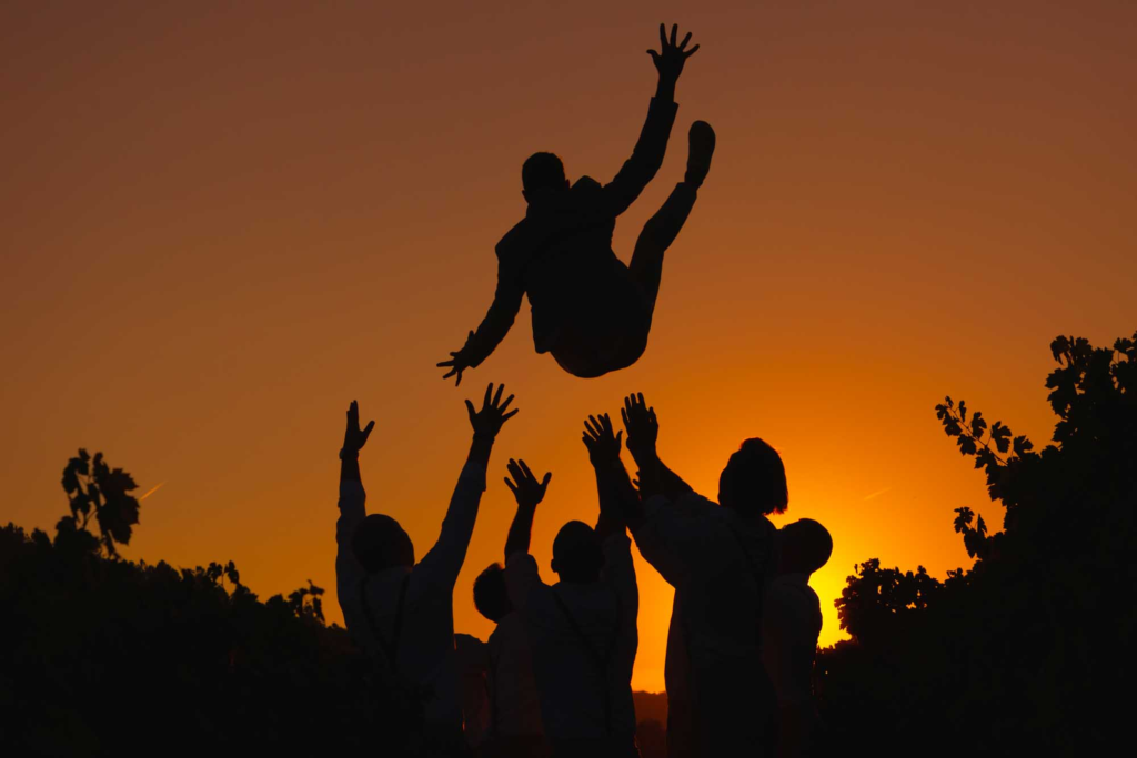 Groom being lifted in the air by friends at sunset, captured in a cinematic style by a Dubai wedding and proposal photographer.