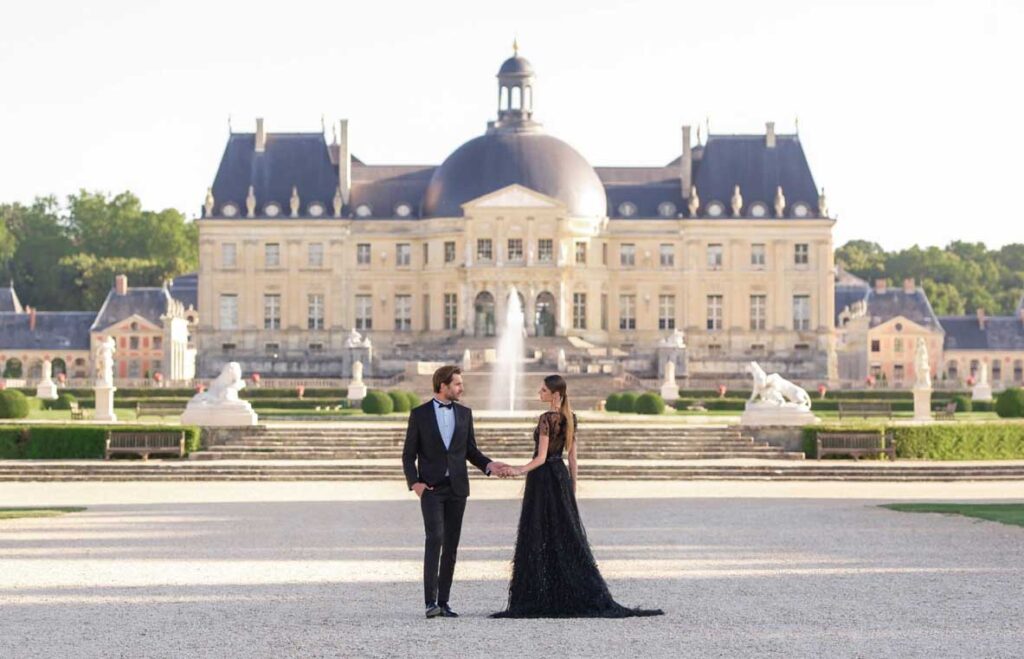 Bride and groom holding hands in front of Château de Vaux-le-Vicomte, captured by a luxury wedding photographer in France