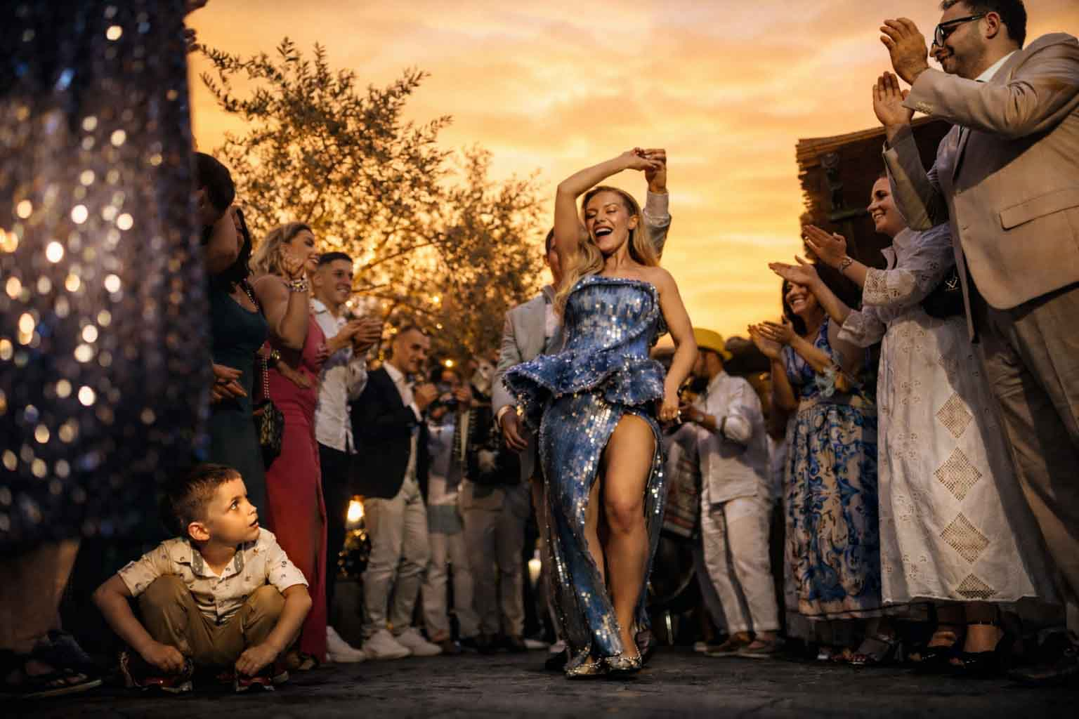 Emotional wedding reception scene in Dubai with the bride dancing at sunset, surrounded by guests, warm light, and a child observing the moment naturally.